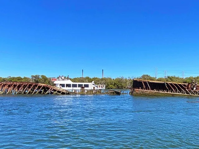 Un bateau de tourisme blanc passant devant les restes rouillés d'une épave