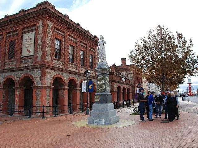 Un groupe de personnes debout près d'une statue devant un bâtiment historique en briques