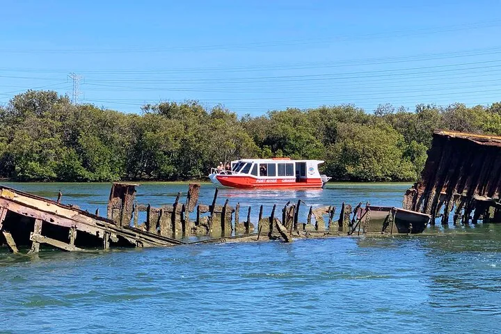 Boot von Port River Cruises fährt an einem langen, rostigen Schiffswrack im Fluss vorbei