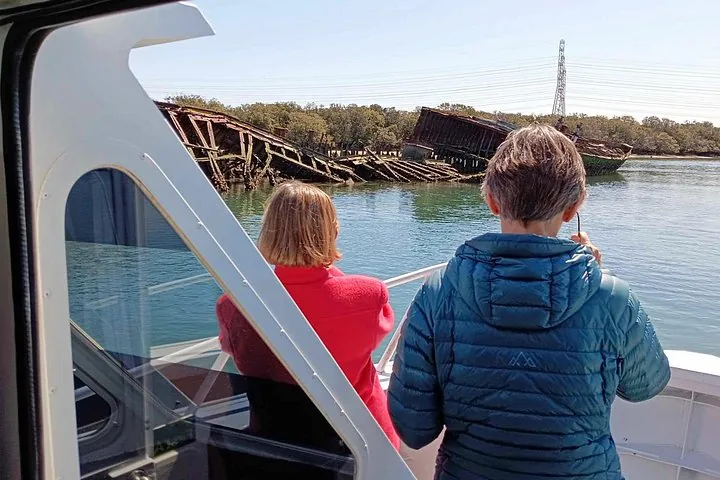 Dos personas en un barco observando un naufragio oxidado en el agua