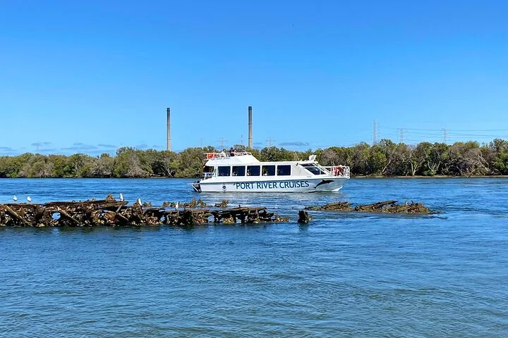 Boot von Port River Cruises fährt nahe einem Schiffswrack und Industrieschornsteinen